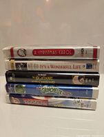 Photo showing stacked VHS tapes of Christmas classic movies including A Christmas Carol, It's a Wonderful Life, The Nightmare Before Christmas, The Grinch (French Version), and Rudolph & the Island of Misfit Toys.