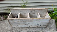 Front view of an antique wooden toolbox with four internal dividers showing worn white paint and some chipping.