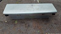 Diamond plated aluminum truck tool box with visible wear and discoloration on top surface.