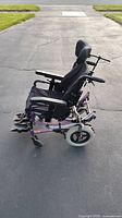 Side view of electric wheelchair showing purple frame, padded black seat, footplates with straps and wheels on pavement