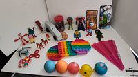 Photo showing full variety of kids toys including pop it toys, balls, fidget spinner, figurines and paper fan arranged on white surface
