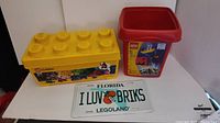 Photo showing two Lego storage containers and the Legoland Florida license plate on a white surface.