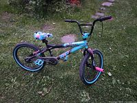 Front side view of the teal and black Tempest kids BMX bike showing the frame, tires, seat, and pedals in daylight and grass background.