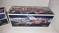 Box artwork showing side of the vintage Hess Emergency Truck with Rescue Vehicle, displaying product features and scenic background.