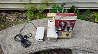 Photo showing a beige and red vintage Riccar RL-343DR Seger lock sewing machine outdoors with power cord and white foot pedal placed on a stone bench.