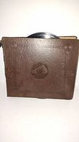 Front of the brown leatherette record album book with a slight part of a vinyl record showing at the top.