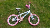 Side view of the girls freestyle bike showing white frame with pink wheels and pedals, peace sign decals on frame.