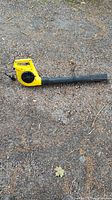Side view of the yellow electric leaf blower lying on gravel.