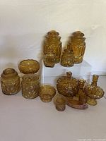 Full view of 15 amber carnival glass items including canisters, jars, bowls, candy dish, candle holders, and decorative pieces.