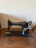 Side view of antique Singer sewing machine showing the full machine mounted on its cabinet, black metal with gold detailing.