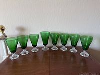 Front view of all eight forest green bubble stemmed goblet glasses on a wooden surface.