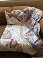 Full view of colorful fan-shaped patchwork quilt folded on a brown couch, showing detailed patterns and colors.