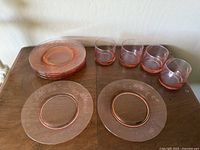 Set of eight etched blush pink glass plates and four matching cups arranged on table.