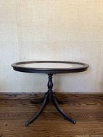 Front view of round mahogany table with glass inset top and lace doily underneath, standing on a central pedestal with four curved legs and claw feet.