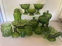 Front view of entire green carnival glass collection showing various items with embossed circle patterns and deep green iridescent finish.