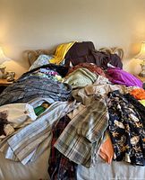 Overview of a large collection of clothing items spread across a bed, showing sweaters, coats, and dresses in various colors and patterns.