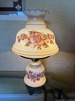Full frontal image of the vintage hurricane lamp showing the cream glass floral shade and base on table.