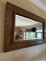 Large rectangular oak framed wall mirror mounted on a beige textured wall reflecting furniture and window in the room.