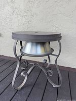 Front angled view of outdoor fire pit showing metal frame with curly legs and metal fire bowl under a solid top.