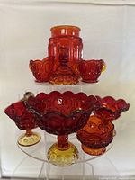 Front view of the red carnival glass lot showing a tall jar, covered dish, creamer, sugar bowl, and footed bowls on a display stand.
