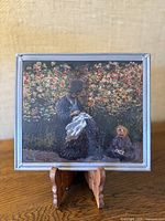 Front view of the stained glass suncatcher placed on a wooden stand, showing the artwork clearly with a floral garden background, a woman and a child seated.