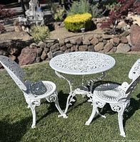 Front view of white cast aluminum bistro table and two chairs on grass