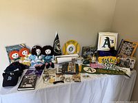 Wide shot showing entire collection of Oakland A's vintage fan memorabilia including caps, dolls, photo frames, pennants, and other items on a tabletop.