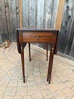 Front view of the vintage wooden drop leaf table with drawer closed.