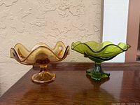 Two vintage glass candy bowls side by side on wooden surface, amber on left and green on right