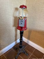 Full view of the vintage red gumball machine on its black metal stand filled with colorful gumballs in a clear glass globe.