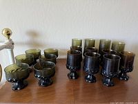 Photo showing full lot of 15 vintage MCM Franciscan Madeira wine glasses by Tiffin Glass Company in olive green and dark smoky colors, arranged on wooden surface.