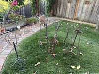 Seven vintage Spanish style iron plant holders arranged outdoors on grass showing various styles and sizes with some rust.