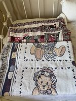 Photo of three folded teddy bear throw blankets stacked, showing fringes and teddy faces on fabric.