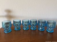 Ten aqua blue Viking Glass lowball glasses arranged in two rows on a wooden surface, showing the honeycomb geometric pattern and vibrant aqua color.