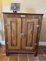 Front view of vintage oak cabinet showing two paneled doors and brass hardware.