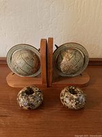 Photo showing two globe bookends made of wooden bases with antique style globes mounted on metal arcs, along with two round candle holders with speckled shell finish placed in front.