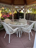 Wicker Hampton Bay patio set under gazebo with round glass table and four white wicker chairs.