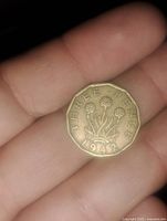 Obverse side of the 1942 England three pence coin showing the inscription 'THREE PENCE' and floral design with the year 1942, held in hand.