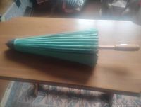 Paper umbrella closed, showing the full length of the turquoise paper canopy, natural wood handle, and dark tip cap.