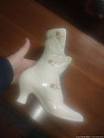 Full view of a cream ceramic vase shaped like a ladies boot with small heel and floral decorations.