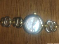 Silver color round Bulova ladies wristwatch with linked band laid flat.