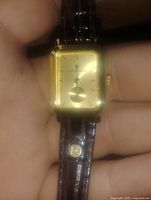 Front view of the rectangular gold-tone watch face with minimalistic design and small seconds sub-dial.