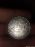 Reverse side of a 1973 Canadian dollar coin showing a voyageur canoe with two paddlers and a bundle of fur with inscriptions.