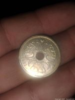 Obverse side of the coin showing symmetrical decorative foliage-like patterns surrounding the central hole