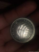 Front side of coin showing raised design of shaking hands.