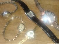 Photo showing seven vintage wristwatches with diverse bands and faces in retro styles.