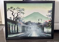 Framed art print depicting a misty street scene with colonial buildings and mountain backdrop, in a black frame.