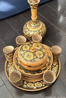 Top view of entire Persian wooden tea set showing vessel, covered bowl, six cups, and tray with black and gold floral patterns