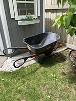 Side view of black Garant wheelbarrow with two handles and single wheel on grassy area.
