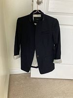 Front view of navy blue blazer hanging on a white door, showing single-button closure and light-colored lining on sleeve cuffs.